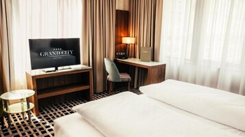Una habitación de hotel con una cama, un escritorio con una silla, un televisor mostrando 