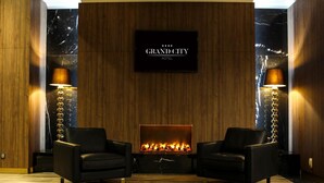 A modern hotel lobby with a fireplace, two leather armchairs, and a sign reading "GRAND CITY HOTEL". - Grand City Hotel Wrocław (Wroclaw)