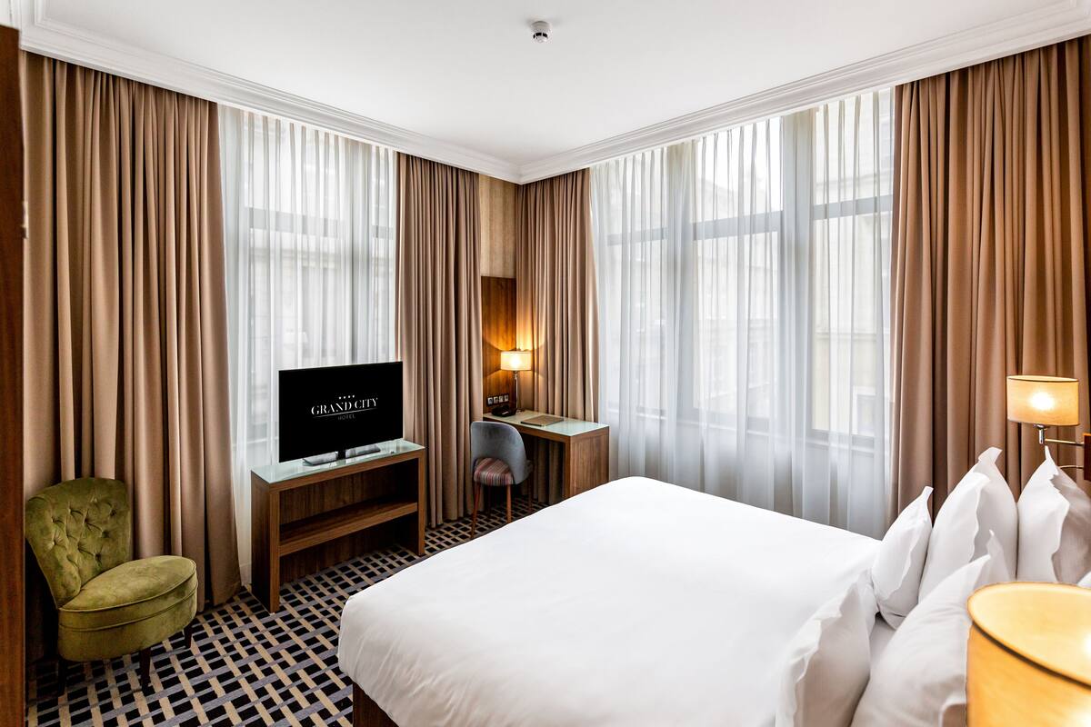A hotel room with a large bed, a desk with a television, a chair, and a lamp.