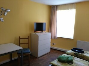 A room with a desk, chair, dresser, and a bed with floral bedding.