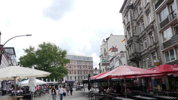 An outdoor café area with tables and chairs, surrounded by cobblestone pavement and historic buildings. - SleepInHamburg St.Pauli Apartment 35&36 (Hamburg)