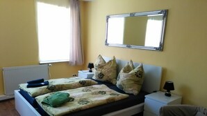 A double bed with floral bedding, two bedside tables with lamps, a mirror above the bed, a radiator, and a window with curtains. - SleepInHamburg St.Pauli Apartment 35&36 (Hamburg)