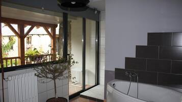 A bathroom with a bathtub, a potted plant, and a view of a balcony.