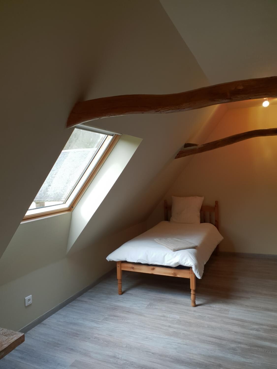 A small, sloped-roofed room with a single bed, a skylight, and exposed wooden beams.