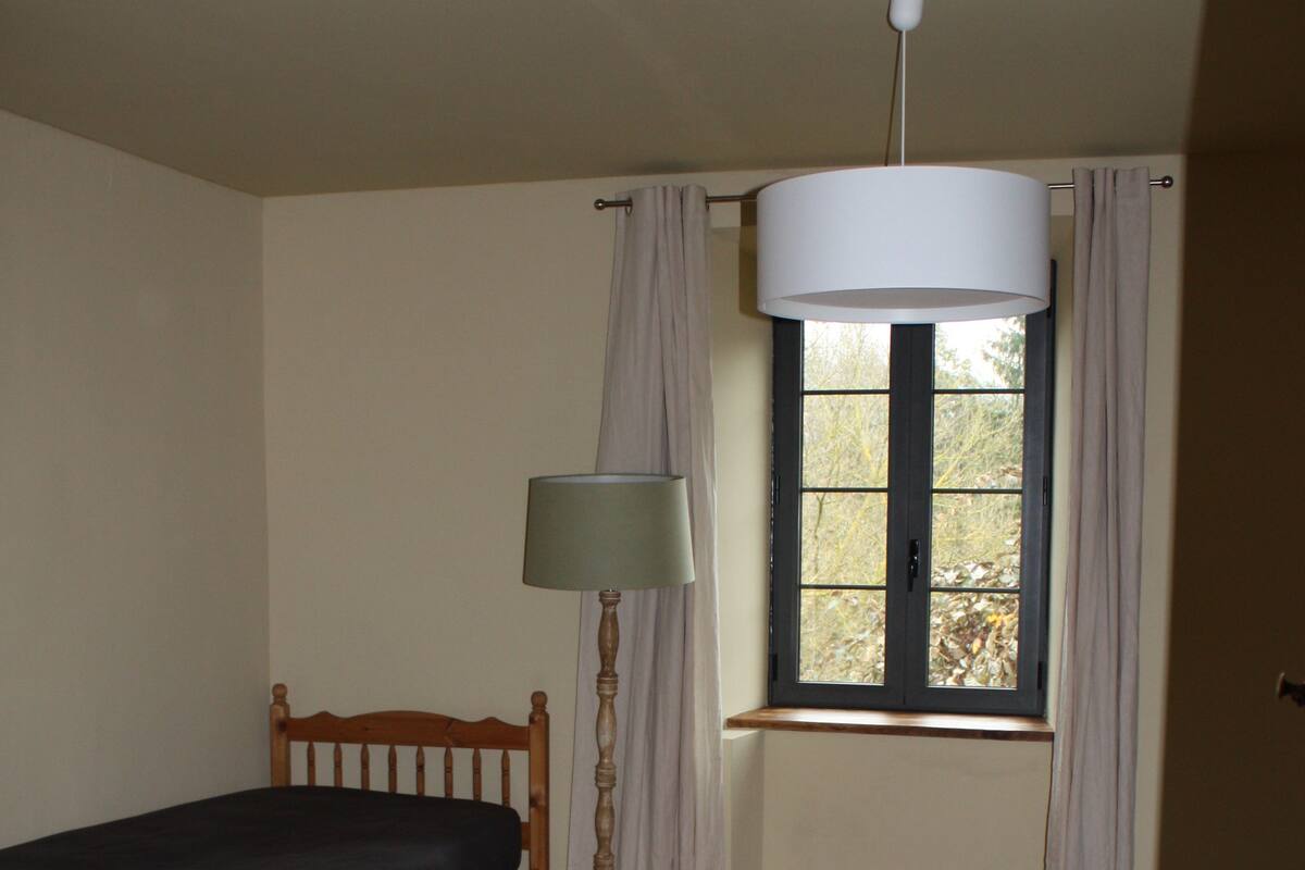 Un dormitorio con cama de madera, ventana con cortinas, lámpara de pie y alfombra.