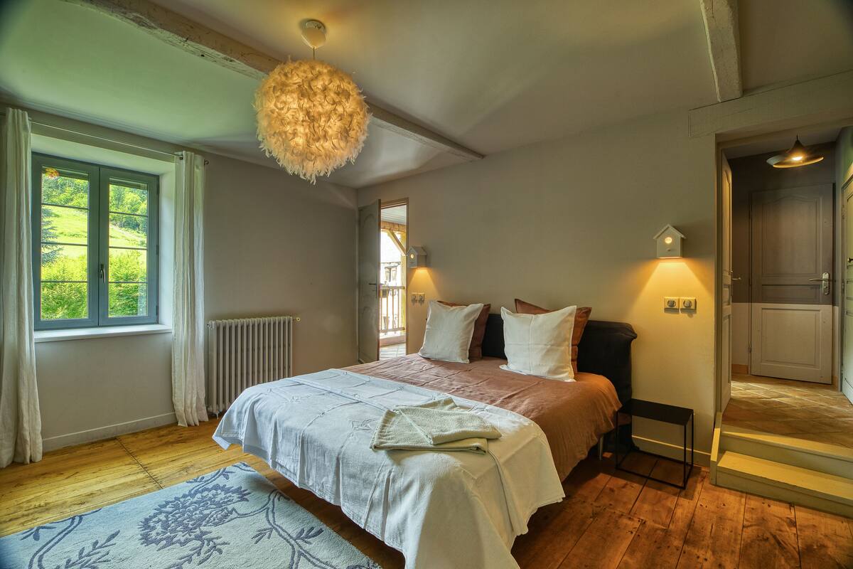 Un dormitorio con una cama grande, una ventana con cortinas, un radiador y una lámpara colgante.