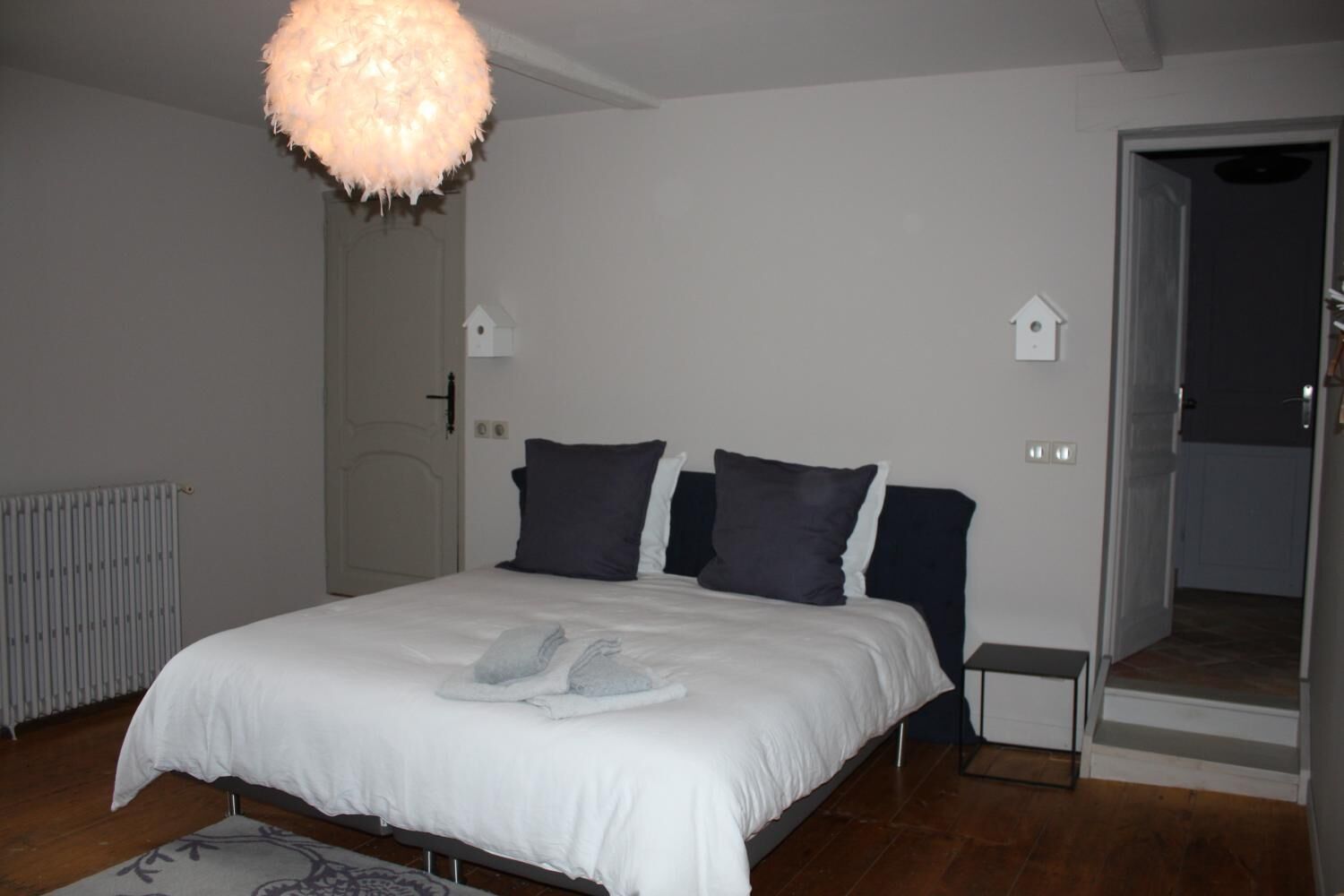 A bedroom with a bed, a radiator, a door, and a small bedside table.