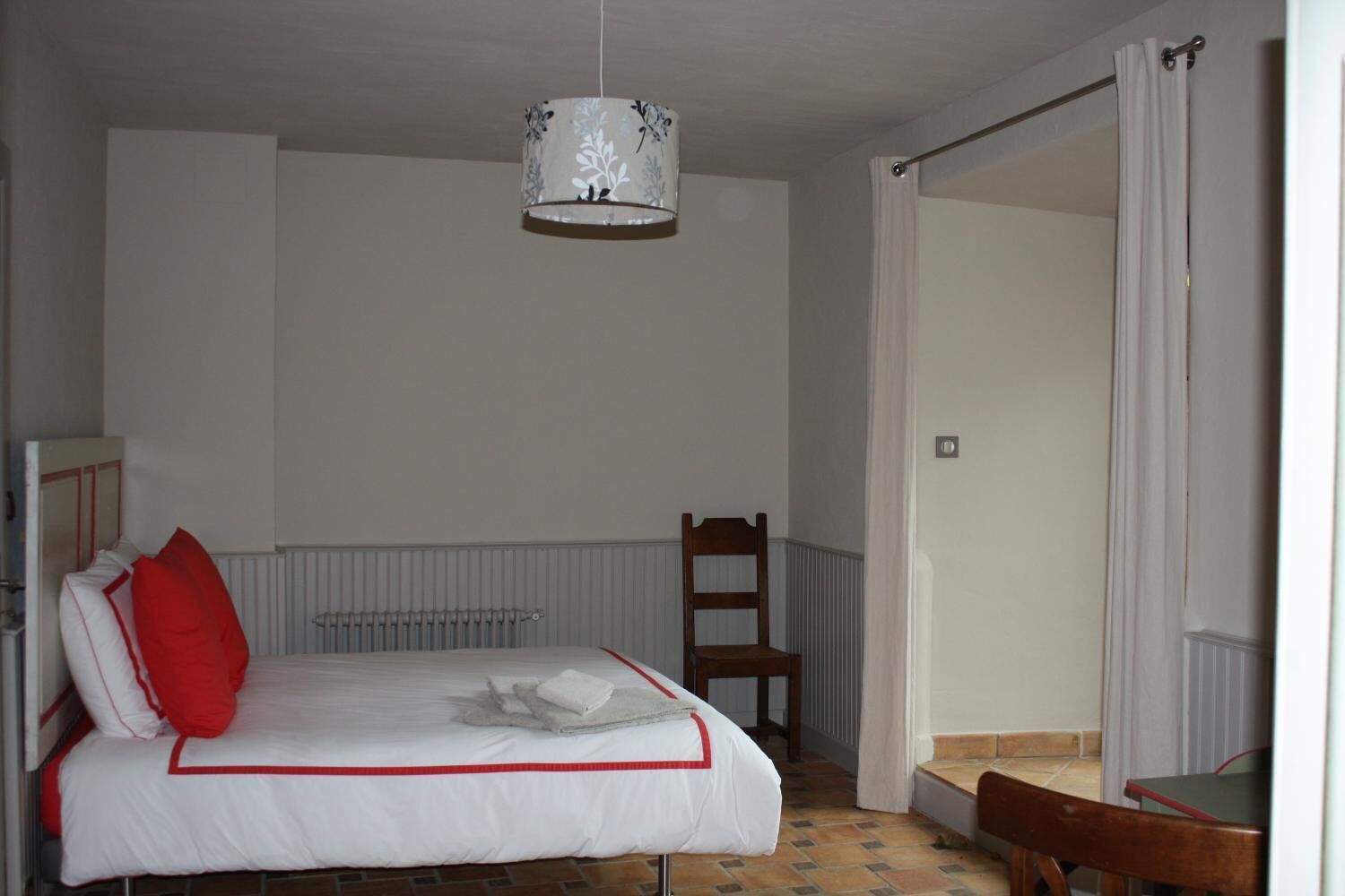 A bedroom with a bed, a chair, a radiator, and a door leading to another room.