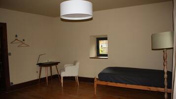 Un dormitorio con cama, escritorio, silla, lámpara colgante, ventana y piso de madera.