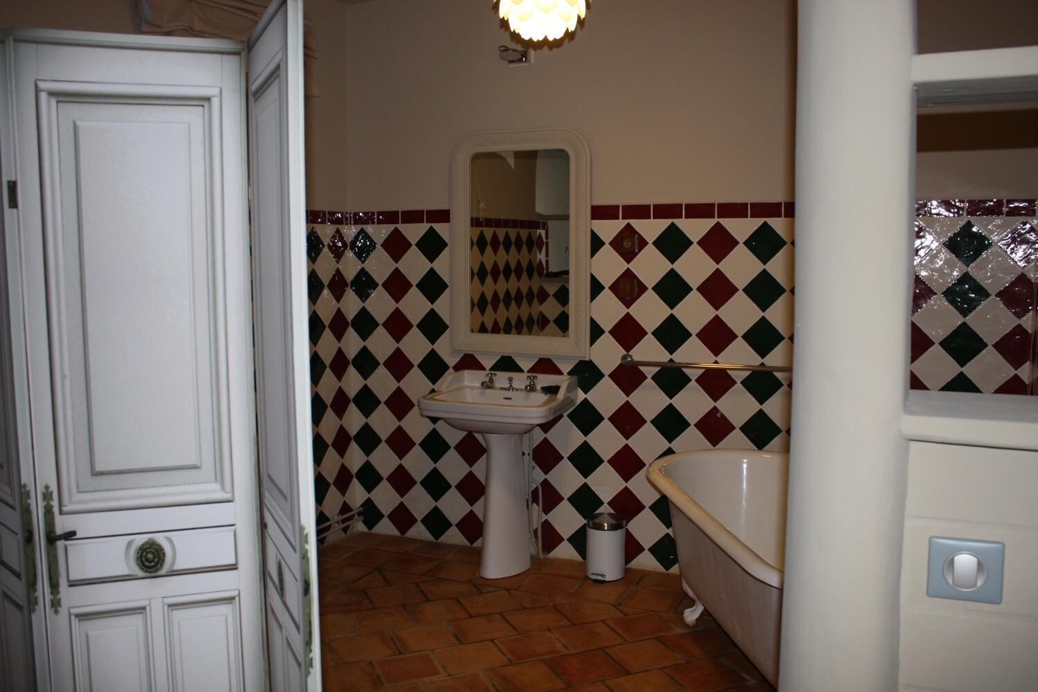 A bathroom with a white door, a sink, a mirror, a bathtub, and patterned tiles.