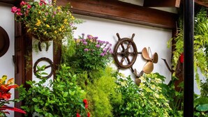 A wall adorned with various plants, a ship's wheel, and a hanging planter. - Hotel Almadraba (Barbate)