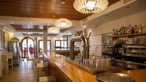 A modern bar area with a wooden counter, bar stools, and a variety of bottles and glasses. - Hotel Almadraba (Barbate)
