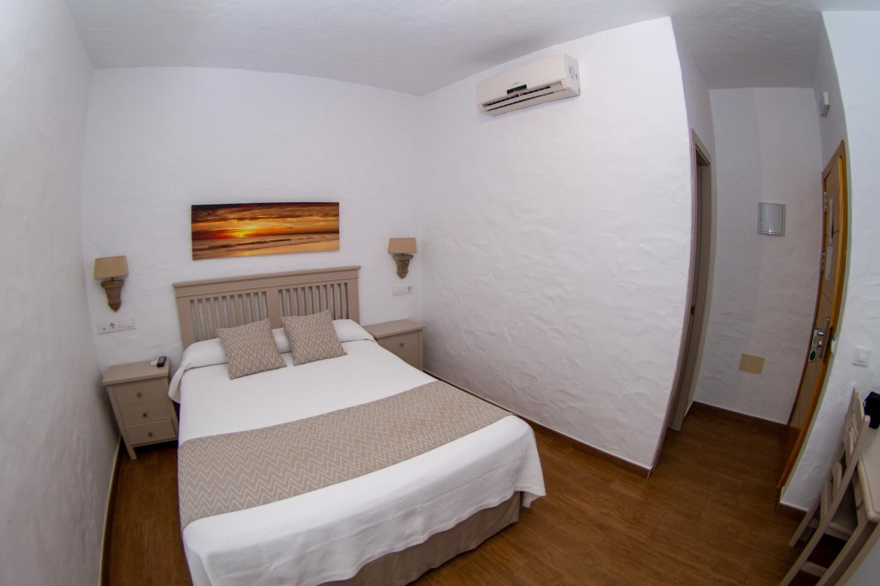 Een slaapkamer met een bed, nachtkastjes, een wandairconditioner en een schilderij.