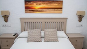 A bedroom with a bed, two nightstands, a wall-mounted lamp, and a sunset painting. - Hotel Almadraba (Barbate)