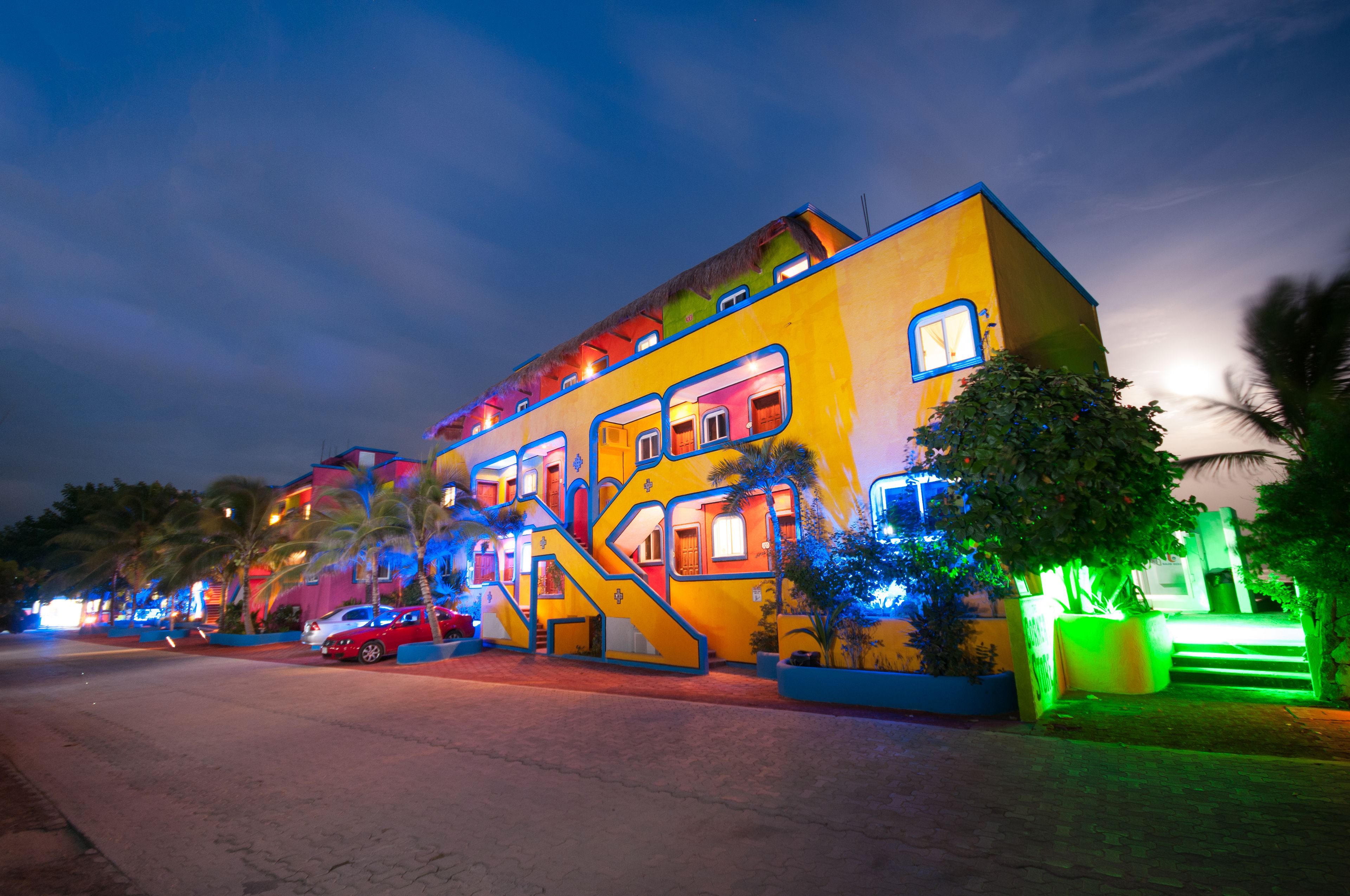 A brightly lit, multi-story building with a unique architectural design, featuring a mix of colors and a visible staircase.