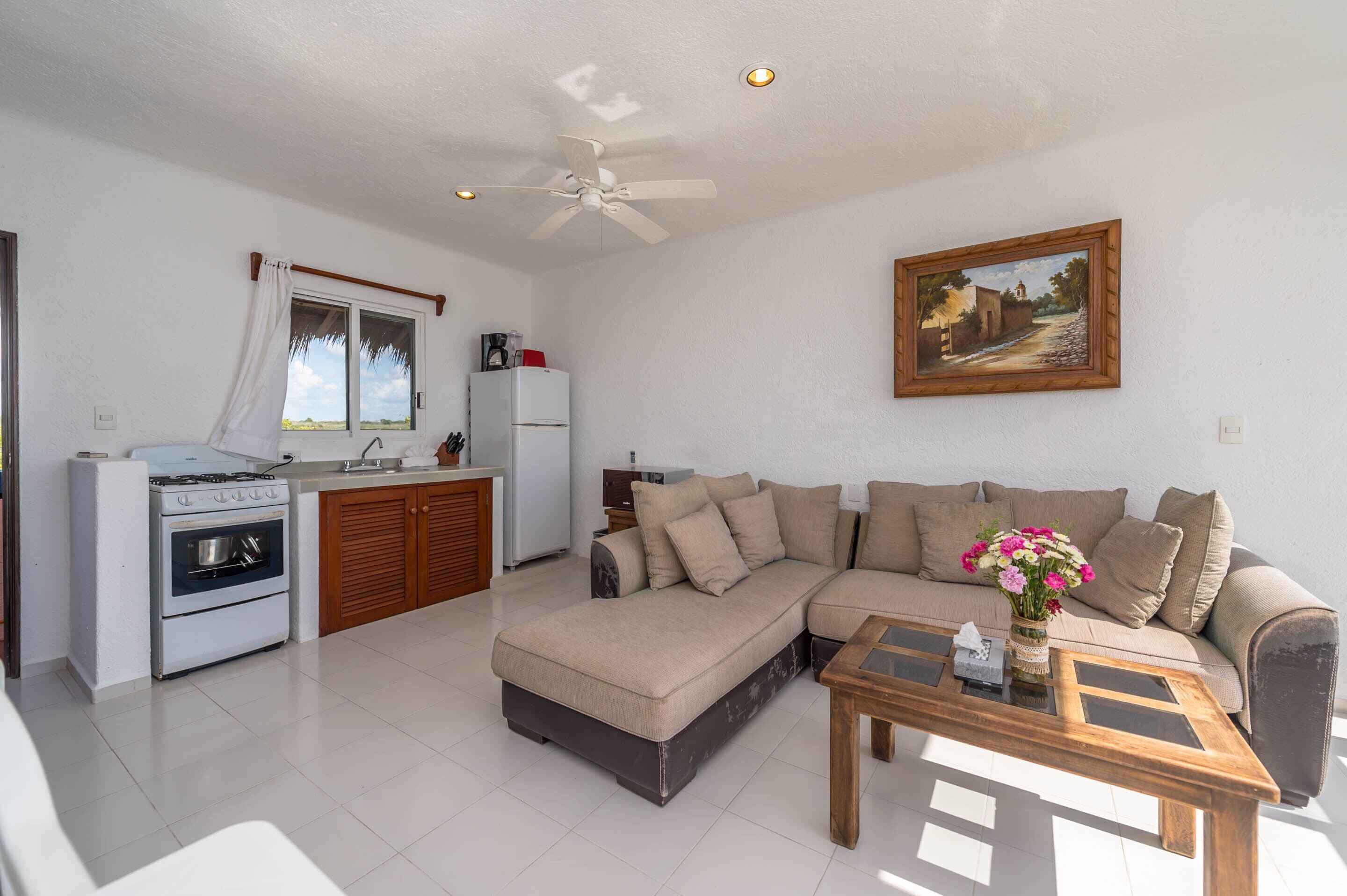 Una sala de estar moderna con sofá, una mesa de centro y una zona de cocina con estufa y refrigerador.
