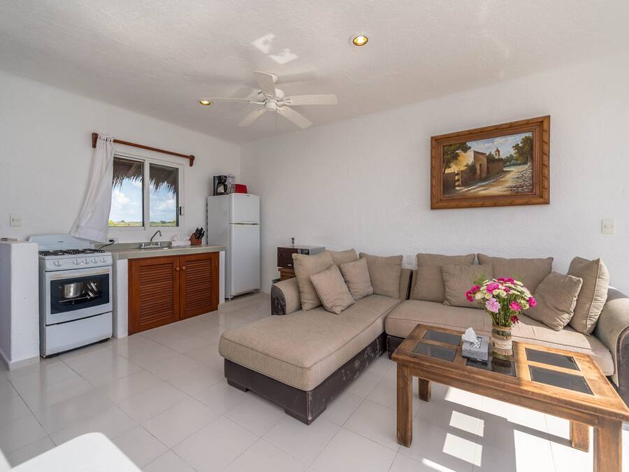 Una sala de estar moderna con sofá, una mesa de centro y una zona de cocina con estufa y refrigerador.