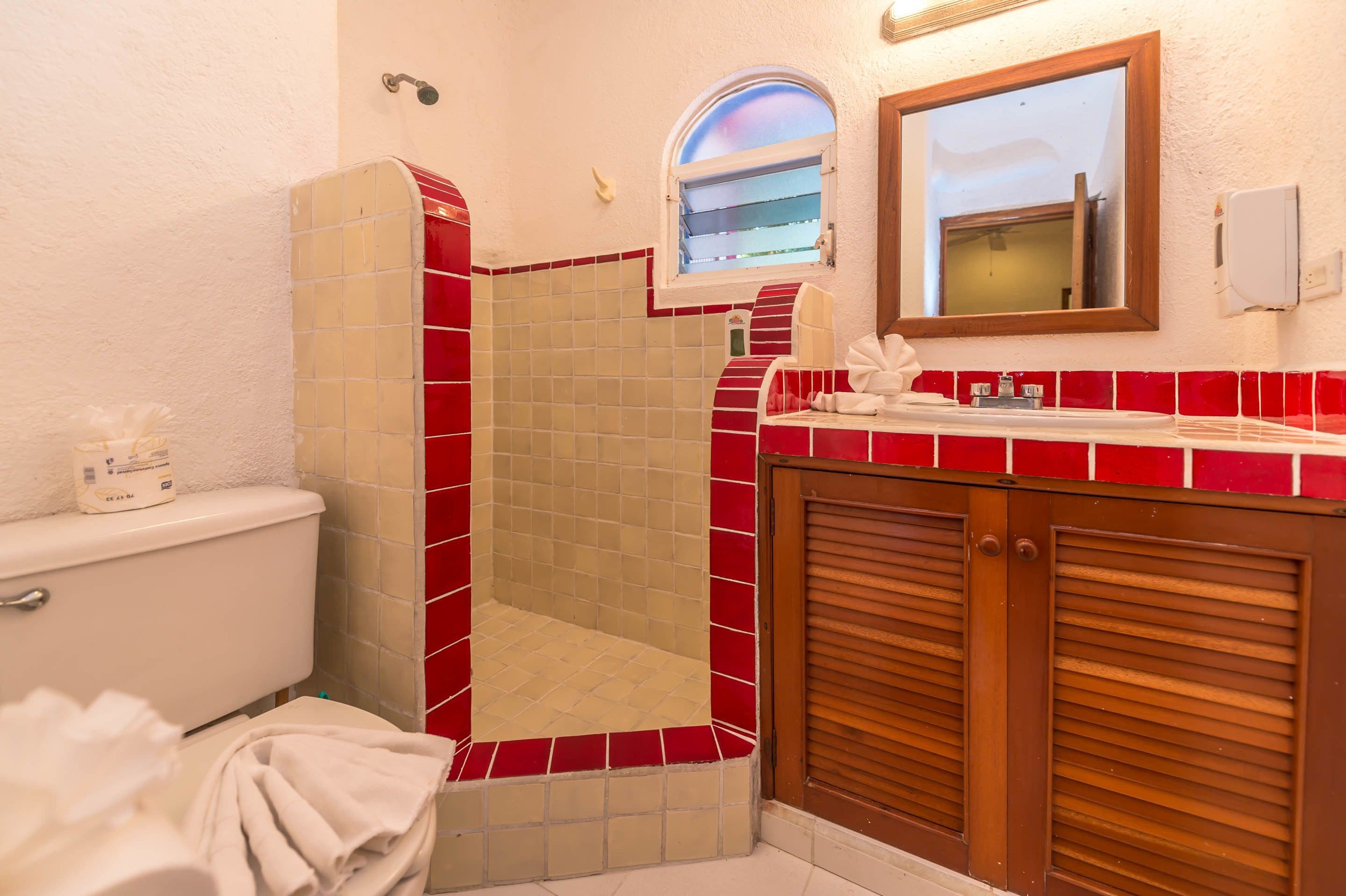 Ein Badezimmer mit einer roten und weißen Duschkabine, einer Toilette und einem hölzernen Waschtisch mit Spiegel.