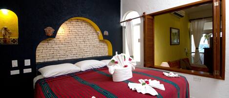A hotel room with a brick-patterned headboard, a red and green striped bedspread, and a large mirror reflecting a window view.