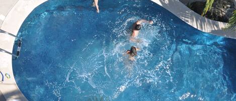 A swimming pool with two people swimming, surrounded by rocks and palm trees.