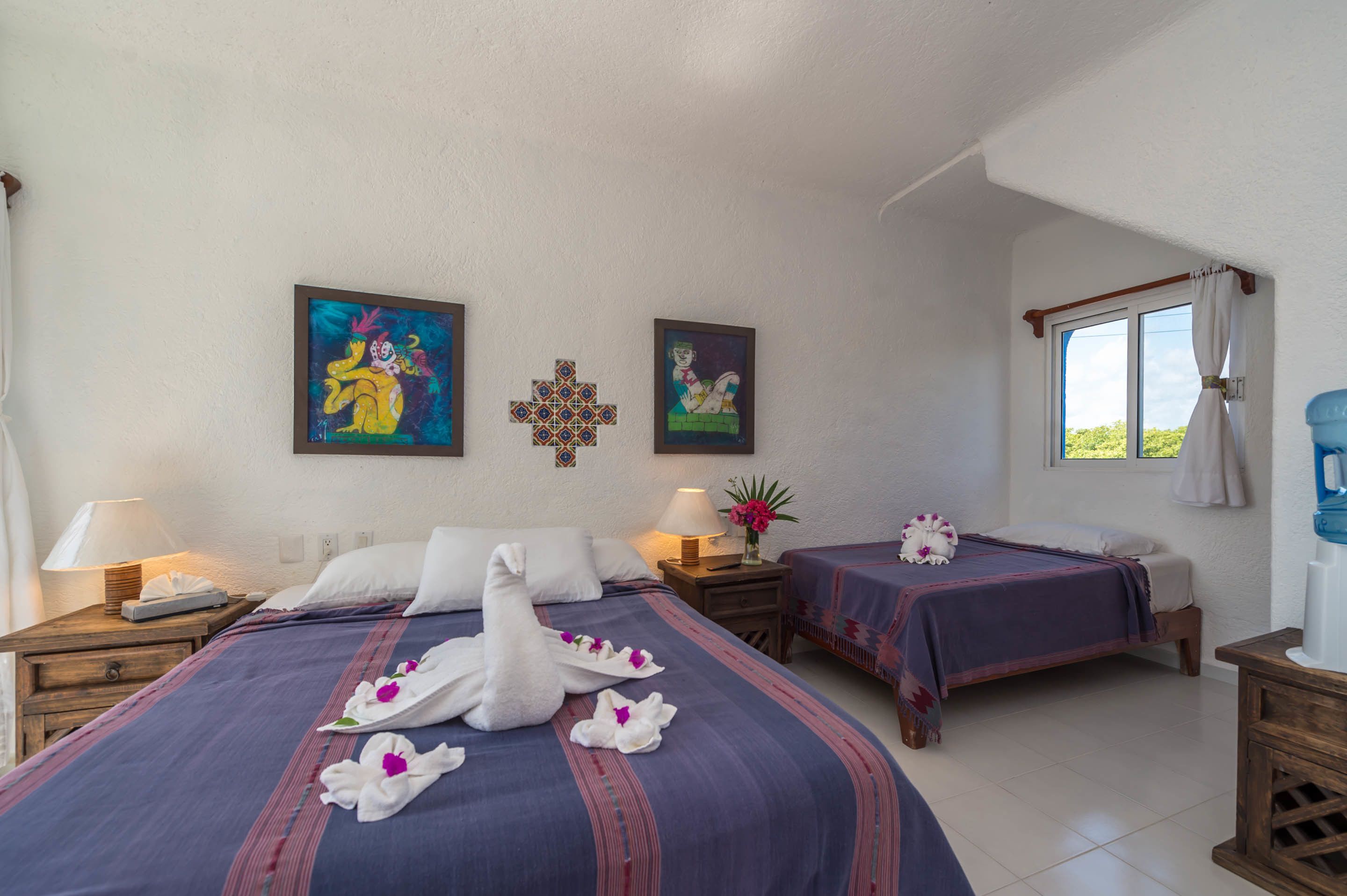 Una habitación de hotel con dos camas, obras de arte en las paredes y una ventana con cortinas.