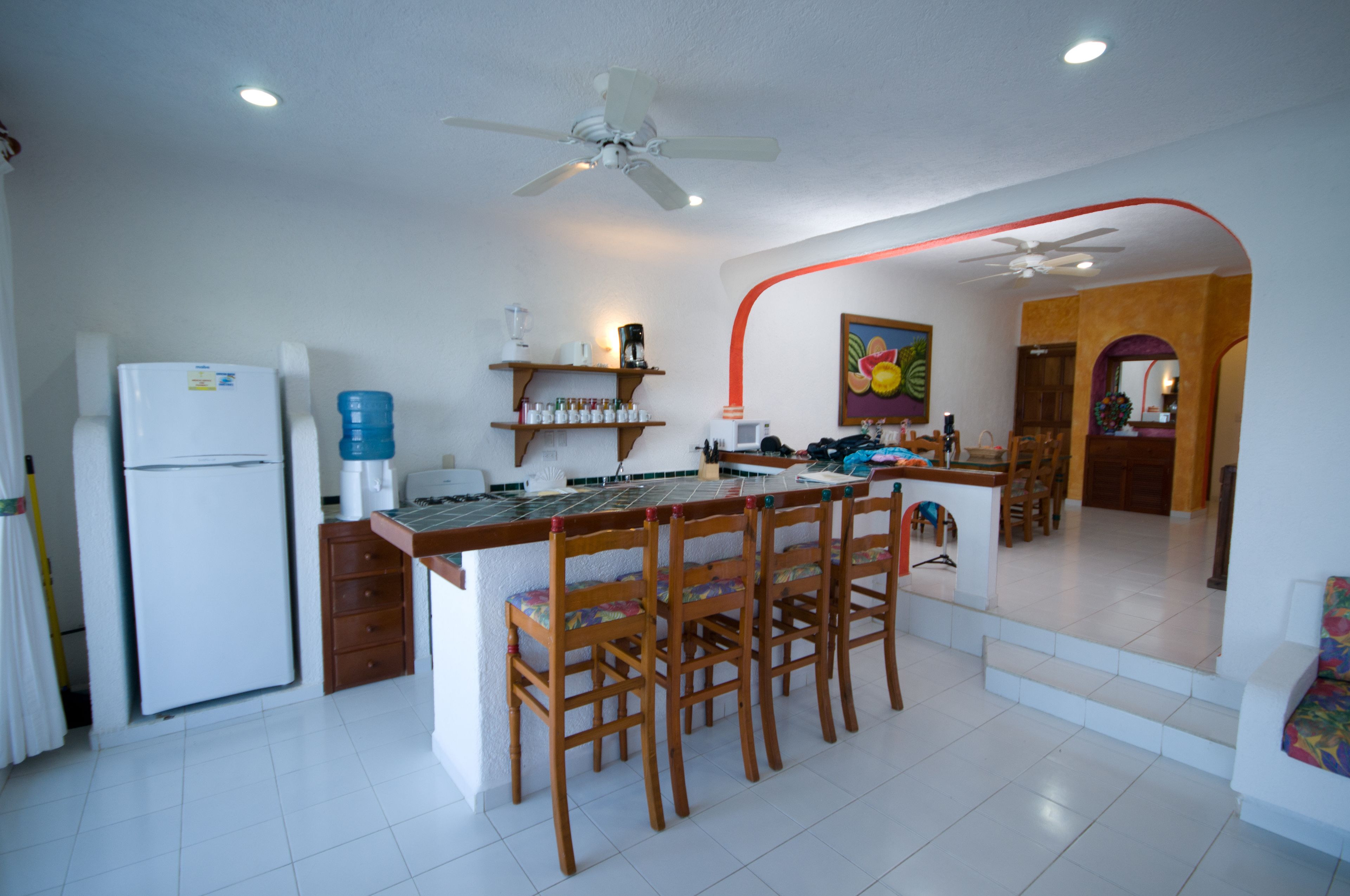 A kitchen with a central island, wooden chairs, a refrigerator, and a ceiling fan.