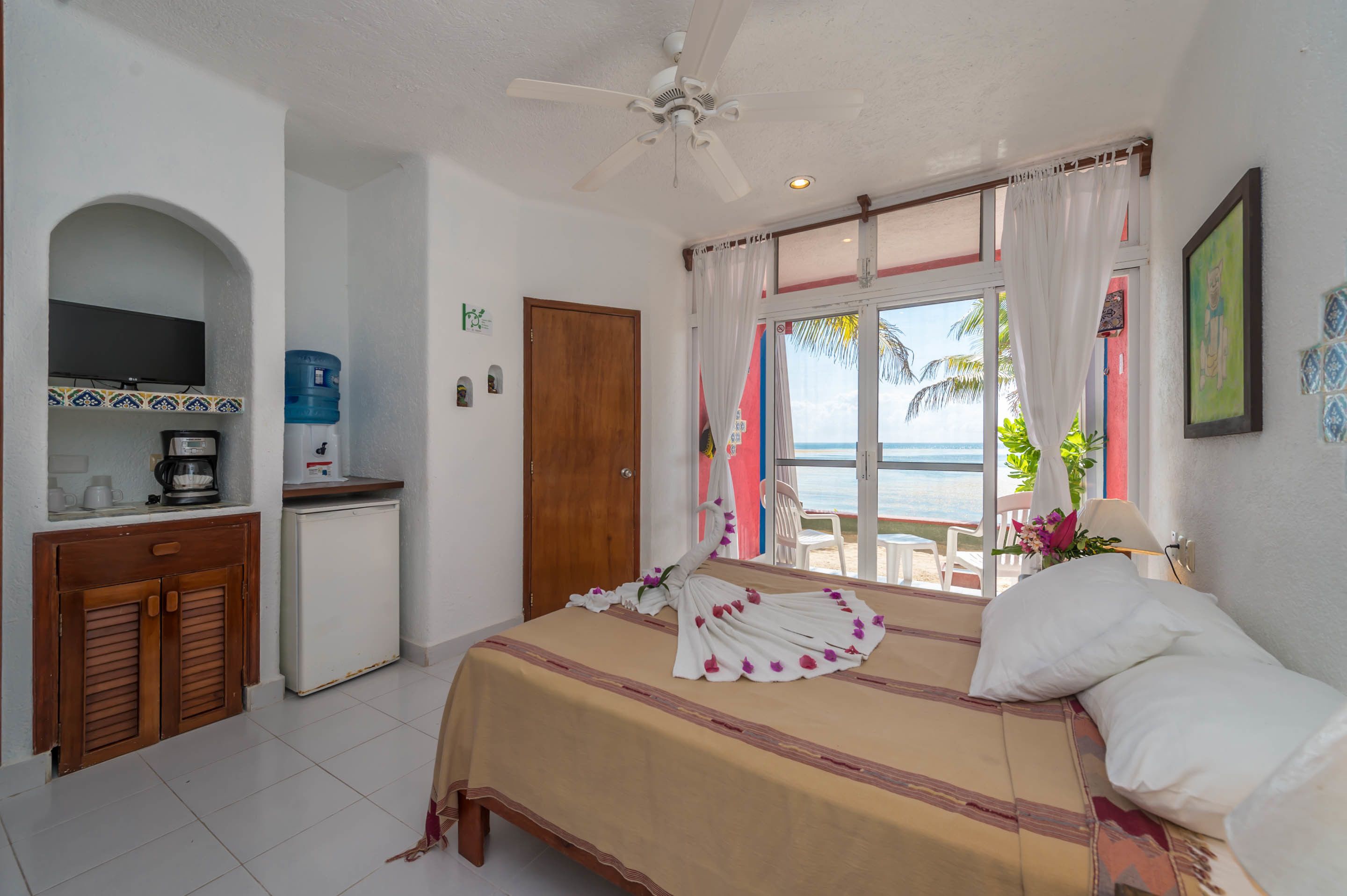Ein Hotelzimmer mit Bett, einer kleinen Küchenzeile, einem Deckenventilator und Blick aufs Meer.