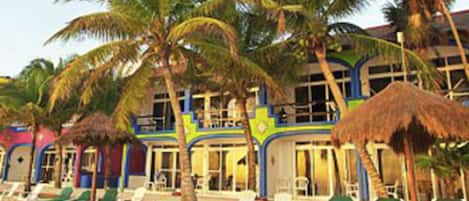 A beachside hotel with multiple balconies, palm trees, and beach chairs.