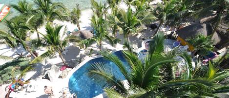 A beach resort with a pool, palm trees, and beach chairs.