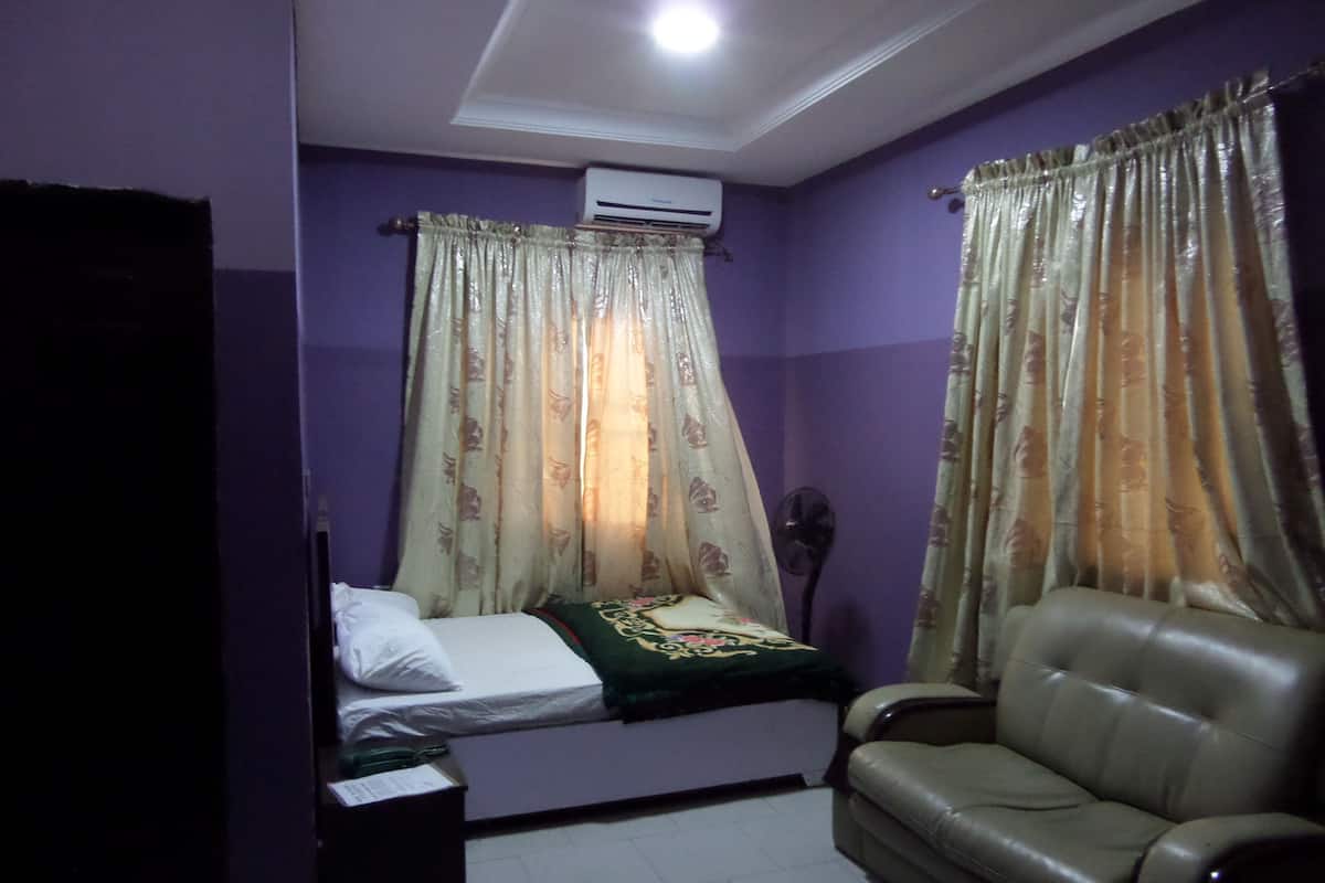 A room with purple walls, a bed with a green blanket, a leather sofa, and a standing fan.