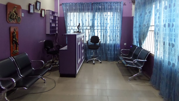 A reception area with a purple wall, a reception desk, and two black chairs. - De Love Hotel (Lagos)
