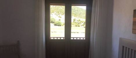 Un dormitorio con cama, ventana con cortinas y vista a espacios verdes.