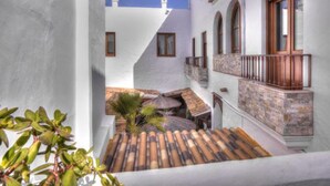 Un patio estrecho con suelo de baldosas, paredes blancas y un balcón de madera.