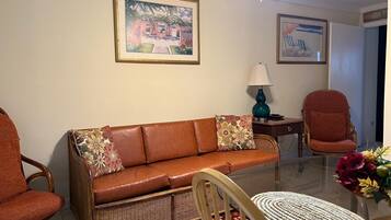 A living room with a brown sofa, a wicker chair, a glass coffee table, and a lamp.