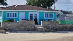 Ein zweistöckiges Haus mit blauer Fassade und weißer Tür, direkt am Strand mit sandigem Strand und Blick auf den Ozean.