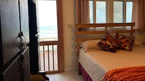 Ein Schlafzimmer mit einem hölzernen Bett, Meerblick durch eine Tür und einem Balkon.