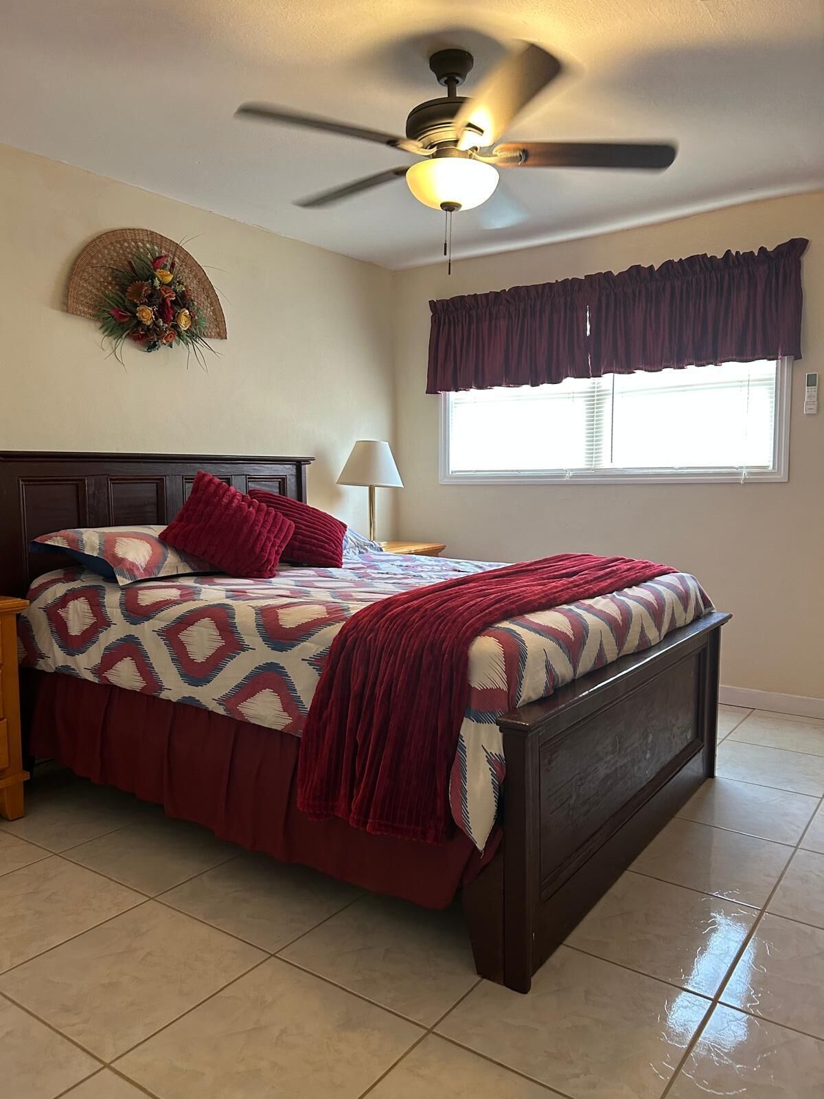 A bedroom with a bed, a ceiling fan, a window with blinds, and a wall decoration.