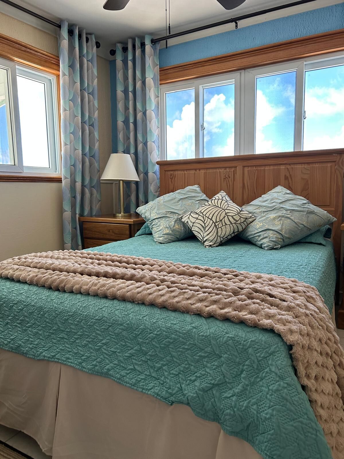 A bedroom with a bed, a nightstand, a lamp, and a window with curtains.