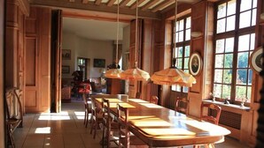 Un'ampia sala da pranzo con un lungo tavolo in legno e sedie, grandi finestre e lampade a sospensione.