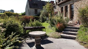 Un edificio in pietra con un patio giardino, caratterizzato da un tavolo rotondo e una panchina.