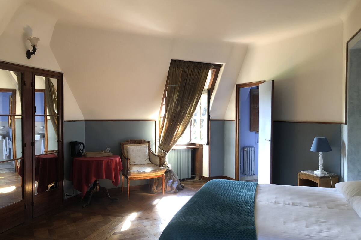 Ein Hotelzimmer mit einem großen Bett, einem Sessel, einem kleinen Tisch mit Wasserkocher, einer Heizung und einer Lampe.
