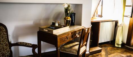 A wooden desk with a vase of flowers, a chair, and a radiator in a room with wooden flooring.