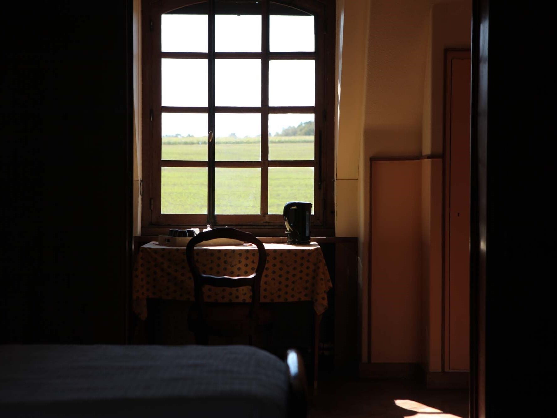 Une pièce avec une grande fenêtre, une table et une chaise, et un lit.