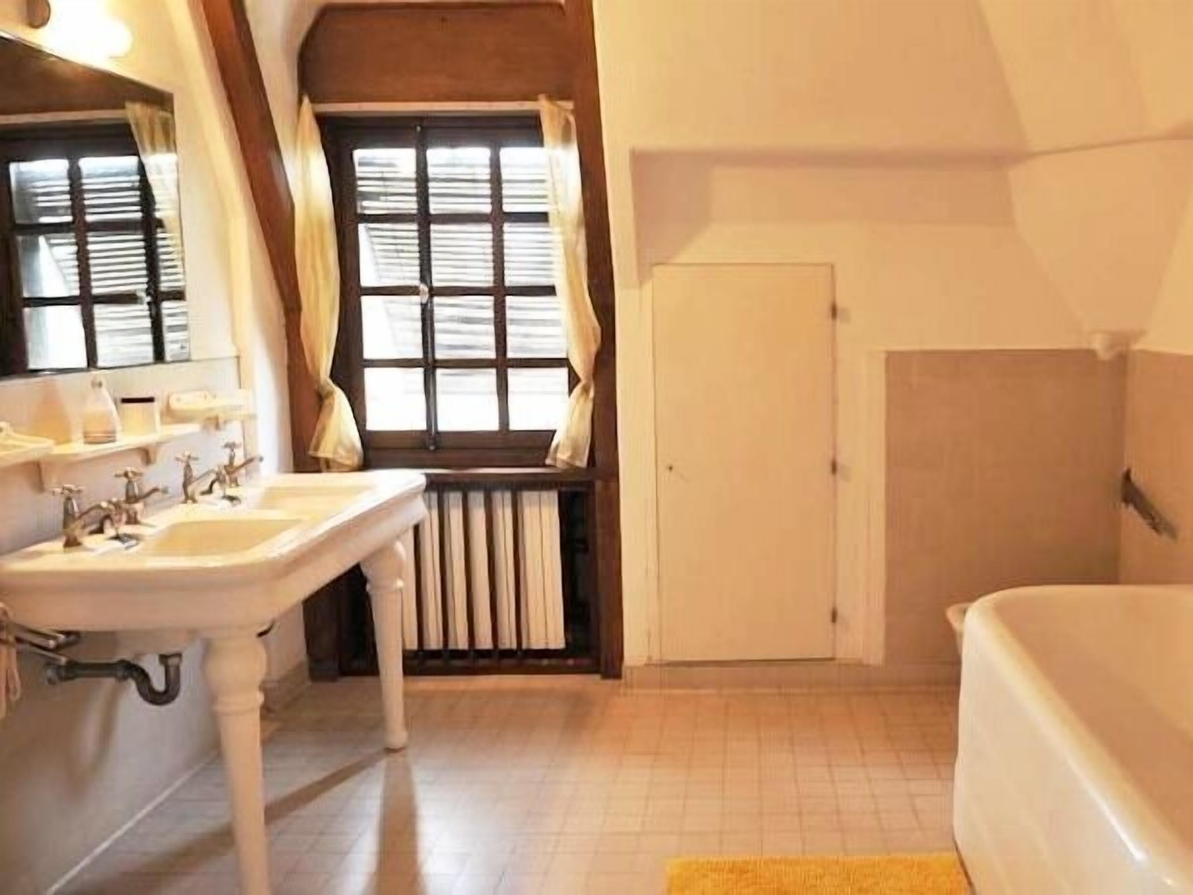 A bathroom with a white sink, a bathtub, and a window with curtains.