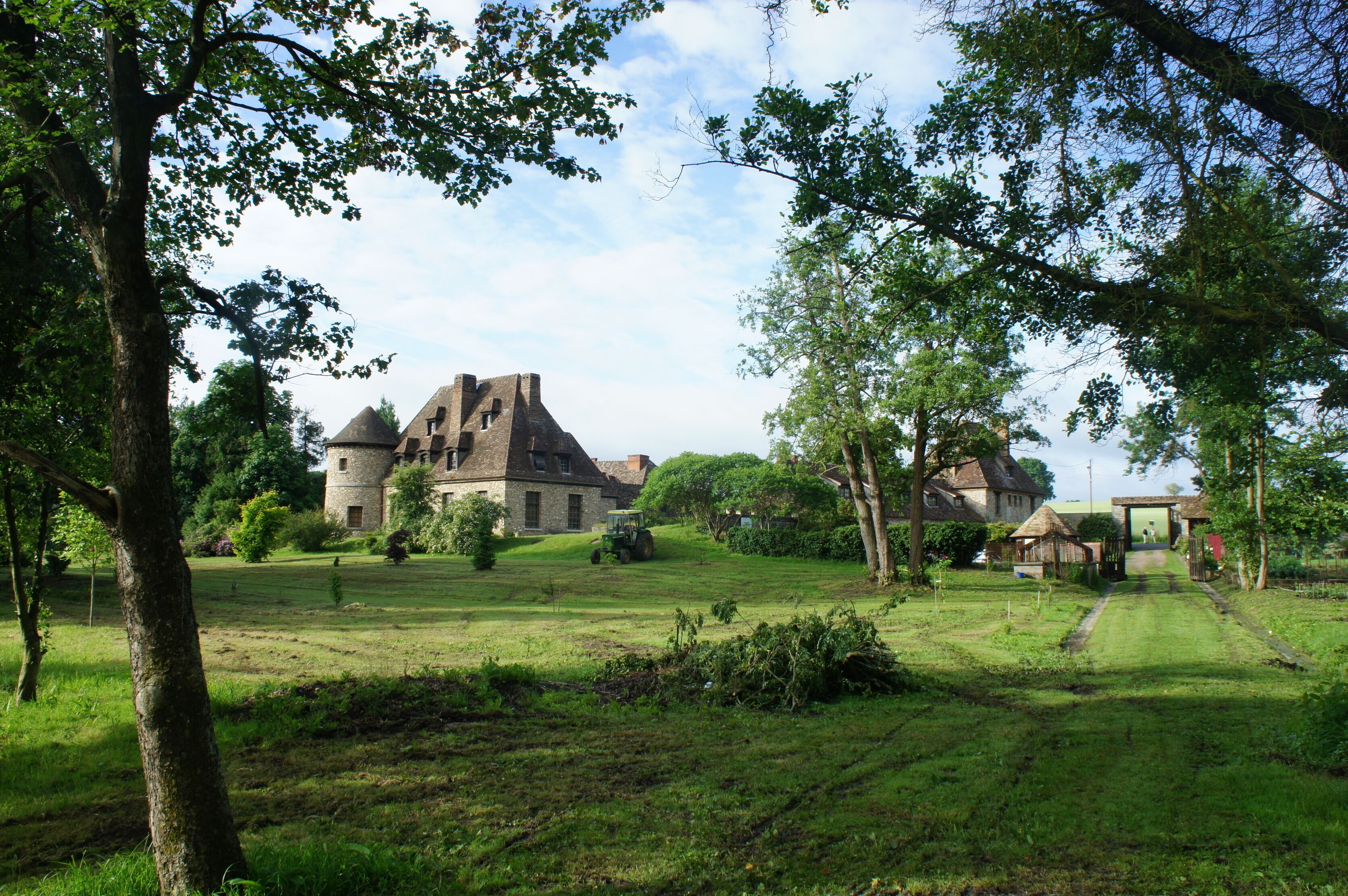 Un bâtiment historique en pierre, doté d’une tour, entouré d’un champ verdoyant et d’arbres.