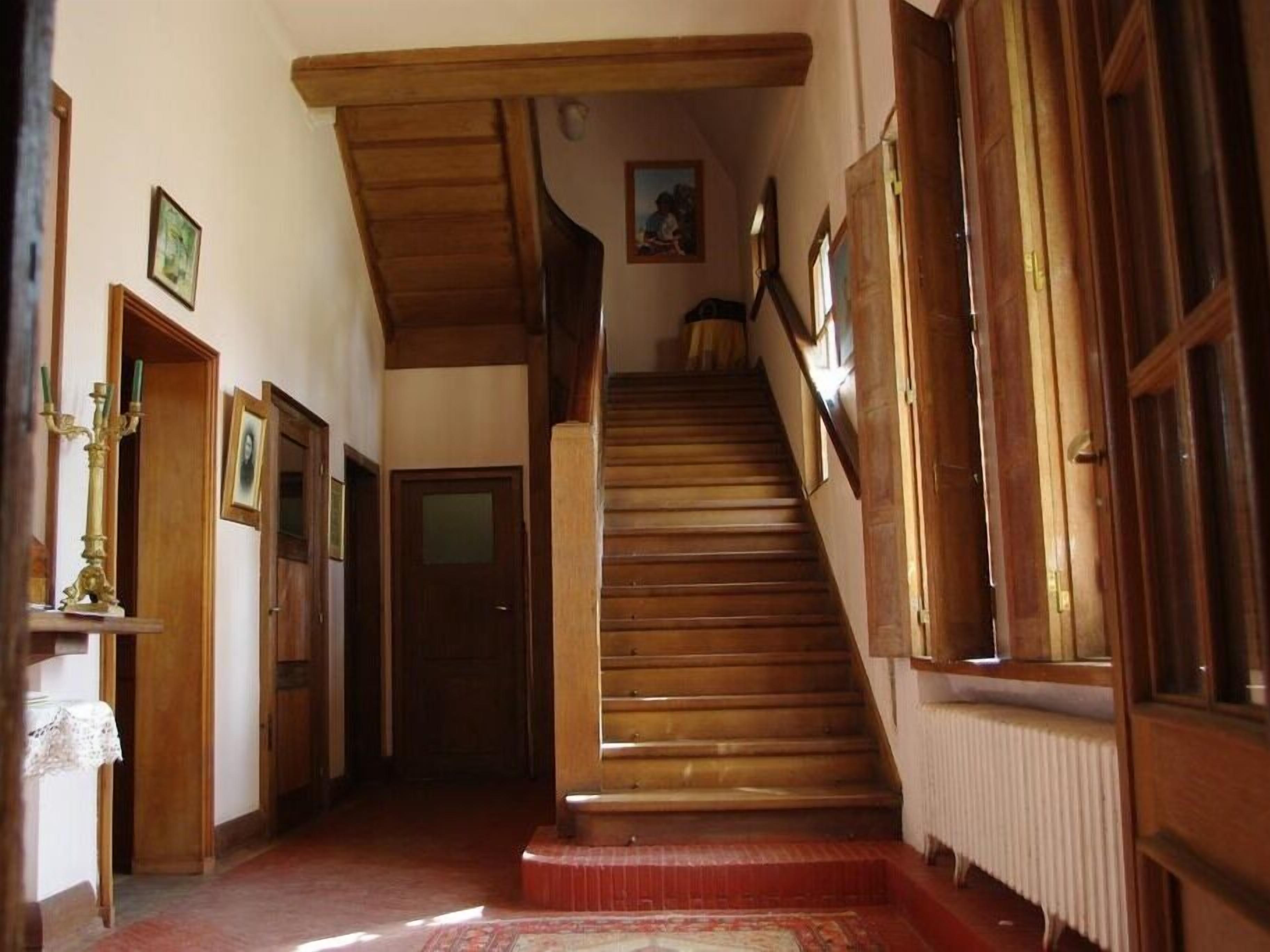 A wooden staircase leading to a second floor, flanked by wooden doors and walls with framed pictures.