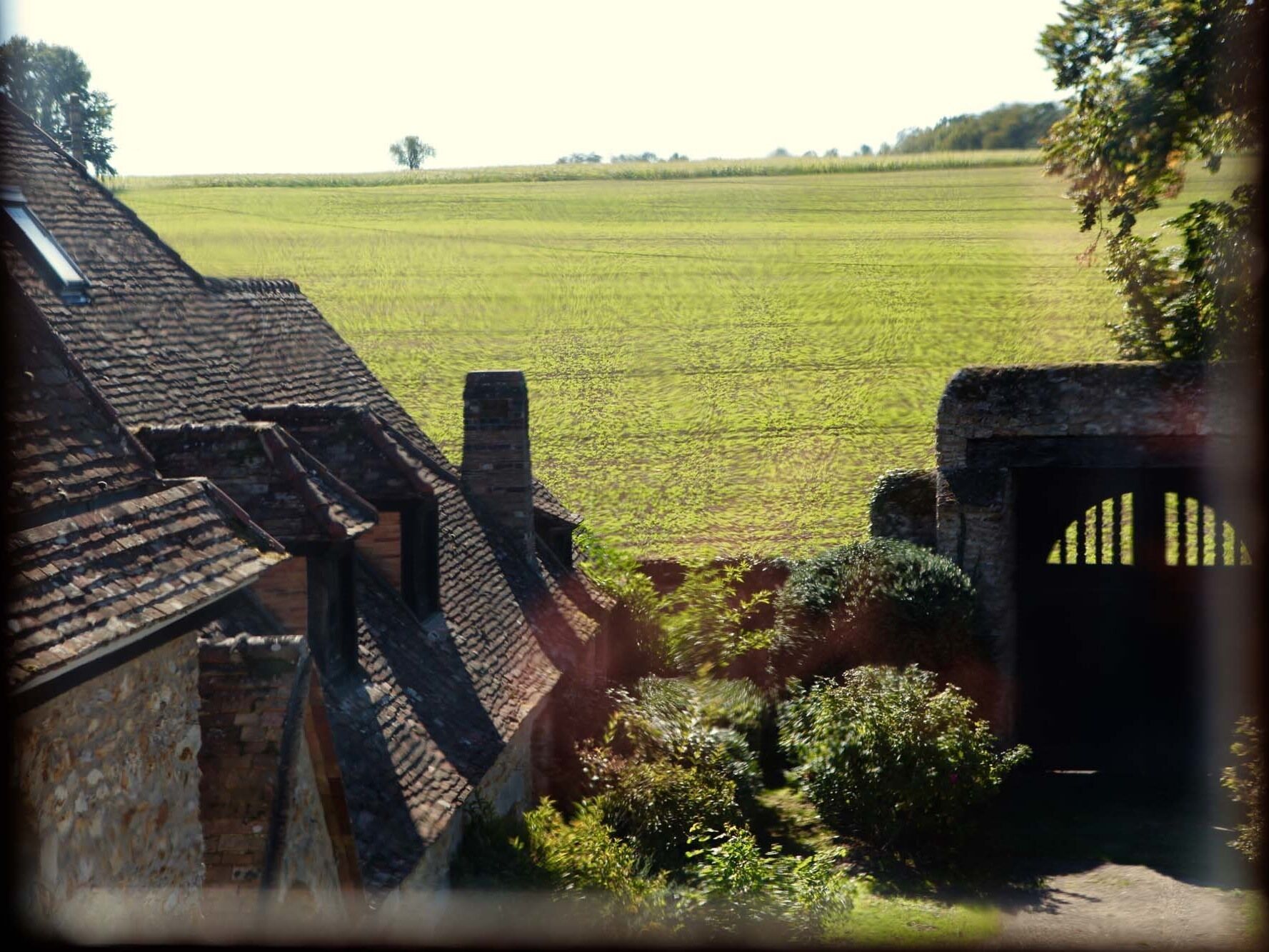 Vista de un paisaje rural con un campo, un edificio de piedra con techo inclinado y una puerta de madera.