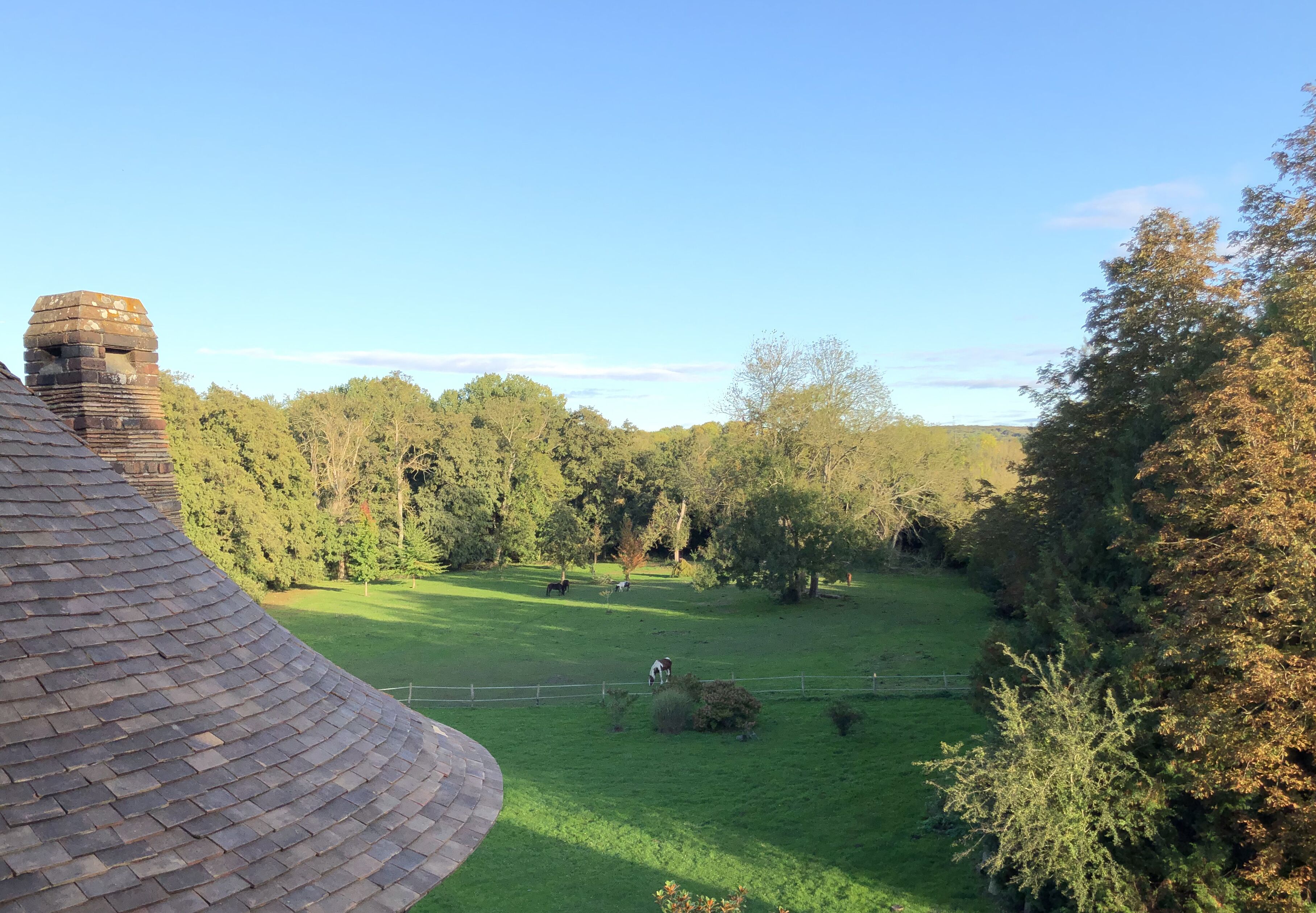 A large, curved brick structure with a chimney, surrounded by a lush green field and dense trees.