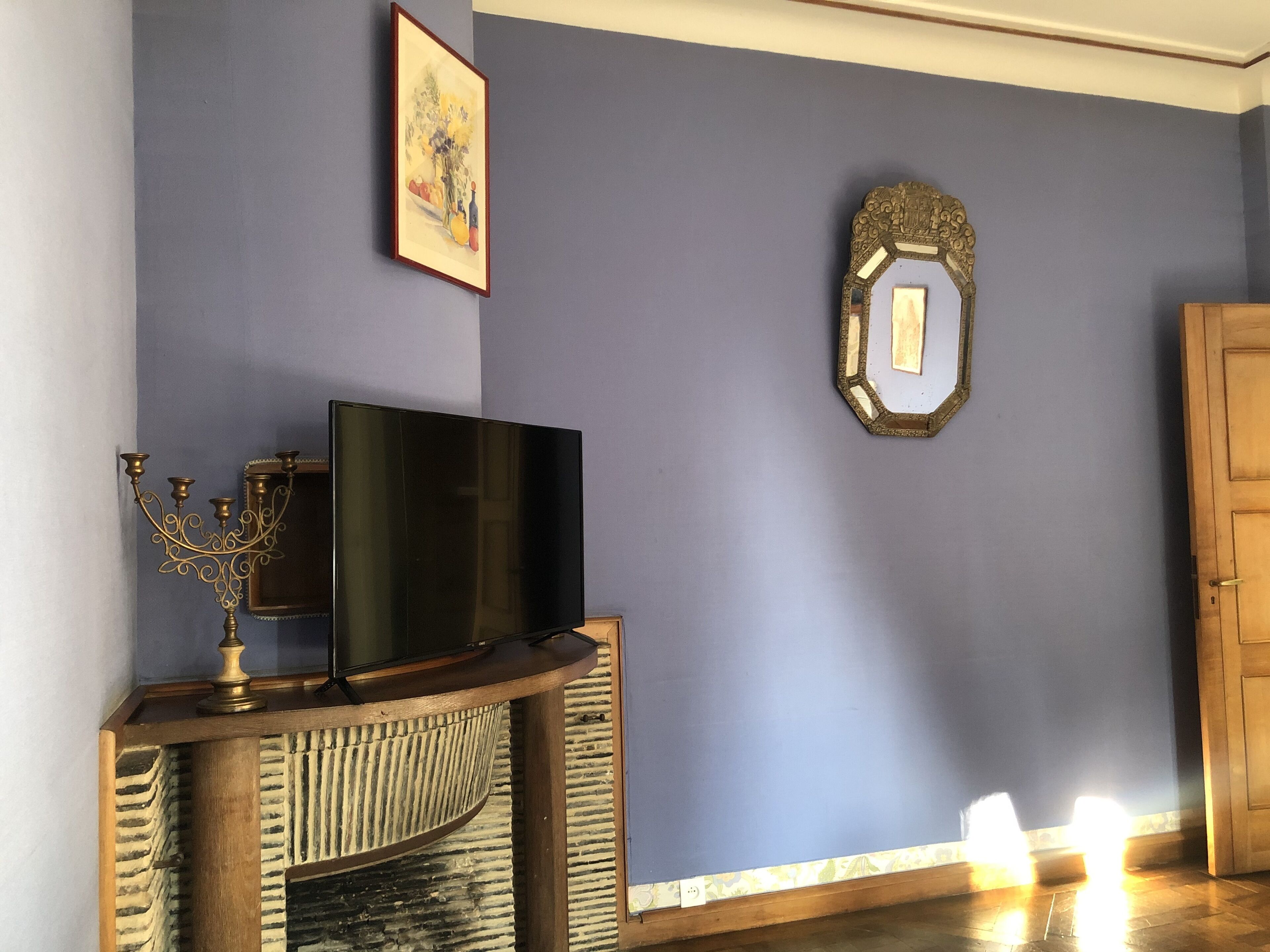 A room with a flat-screen TV on a wooden stand, a decorative candelabra, a framed artwork, and a mirror on the wall.