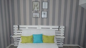 Una cama blanca con cabecera a rayas, dos almohadas y una mesita de noche.